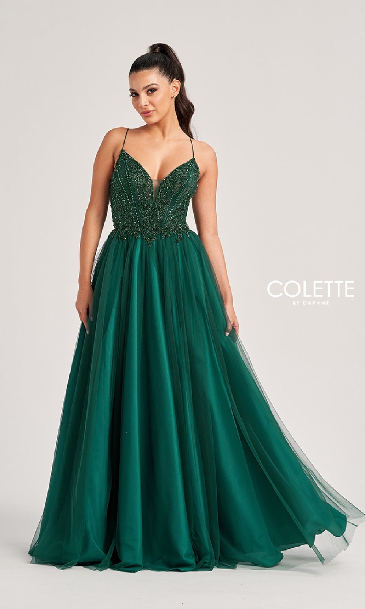 A woman stands against a plain background in the Colette CL8250 Long Prom Dress, featuring a dark green sequin bodice with thin straps and a full beaded tulle skirt for an elegant, floor-length look.